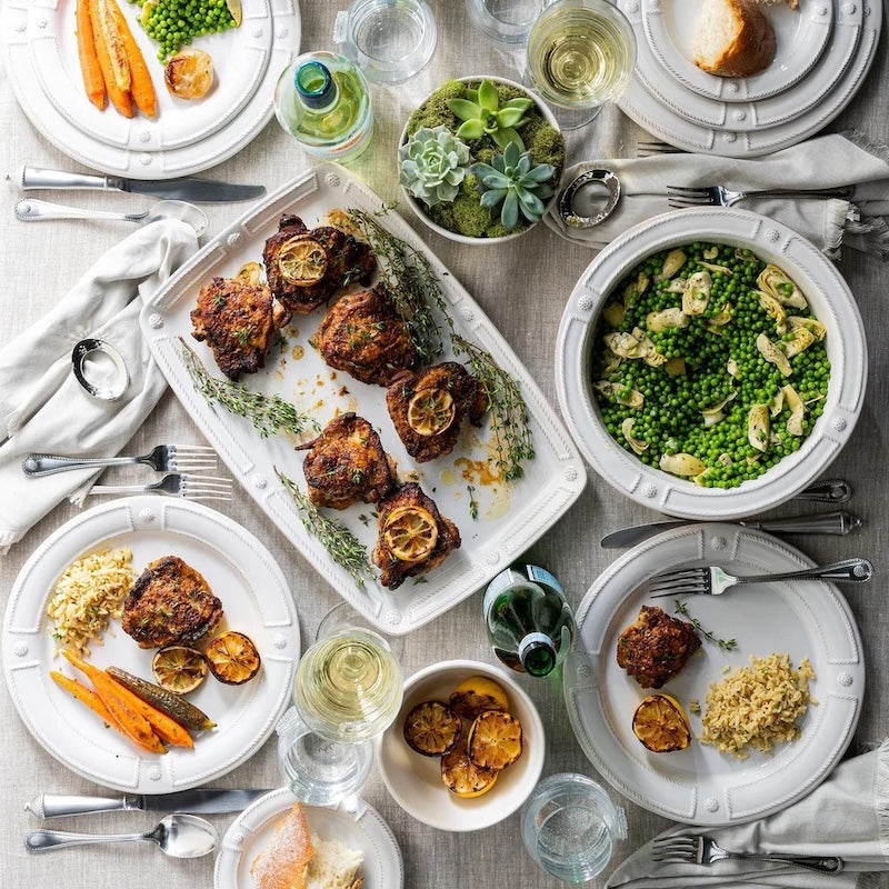 Image of a table set with serving plates full of food and dinning-ware and cutlery